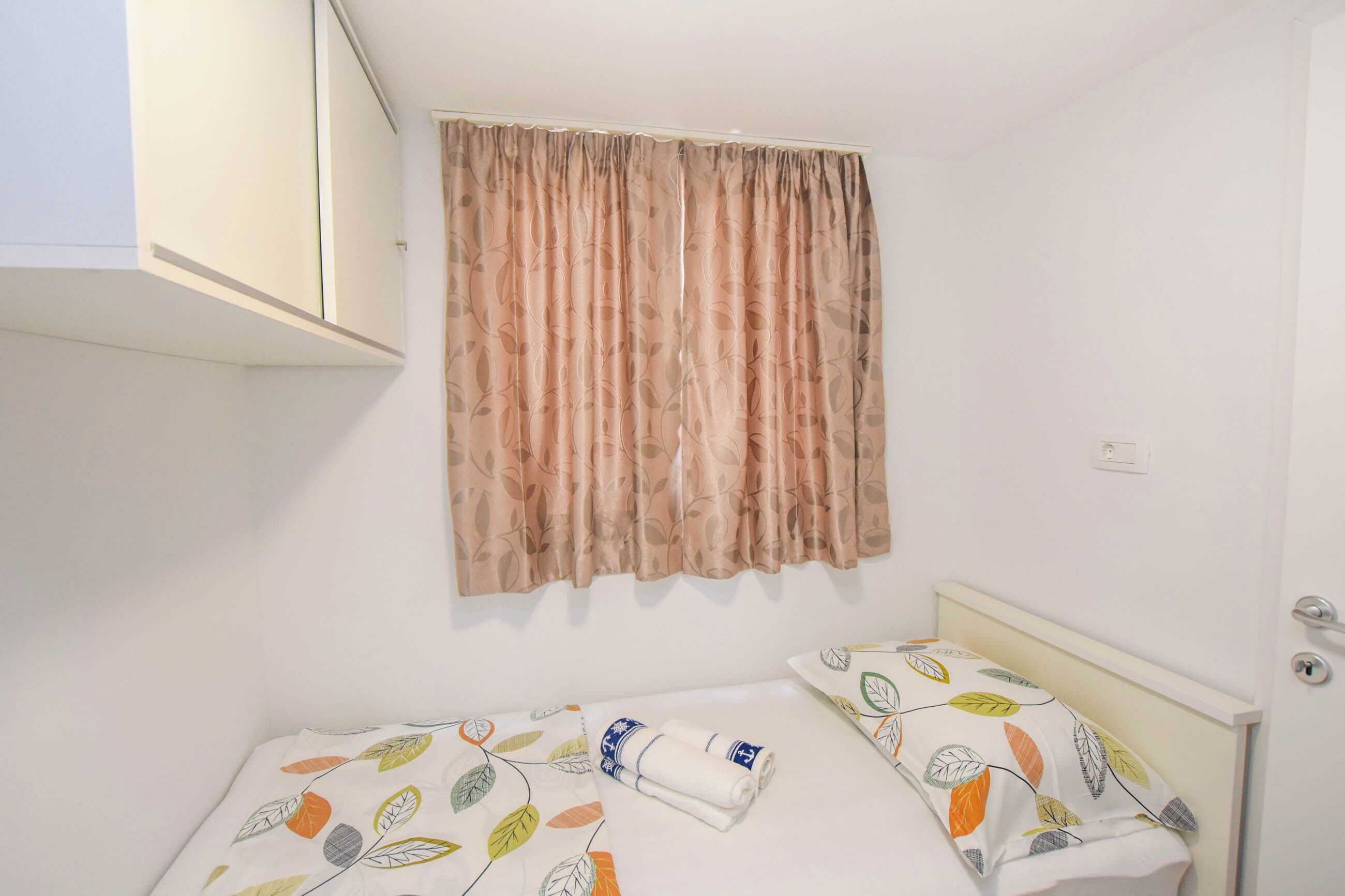 Een kleine, schone kamer met een bed, een raam met gordijnen en een deur.