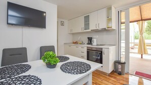 A modern kitchen with white cabinets, a flat-screen TV, and a dining table with black placemats and a potted plant. - Mobile Home Dandelion (Biograd na Moru)