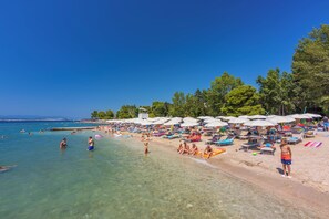 A beach with clear water, umbrellas, and people relaxing. - Apartments Daniela (Crikvenica)
