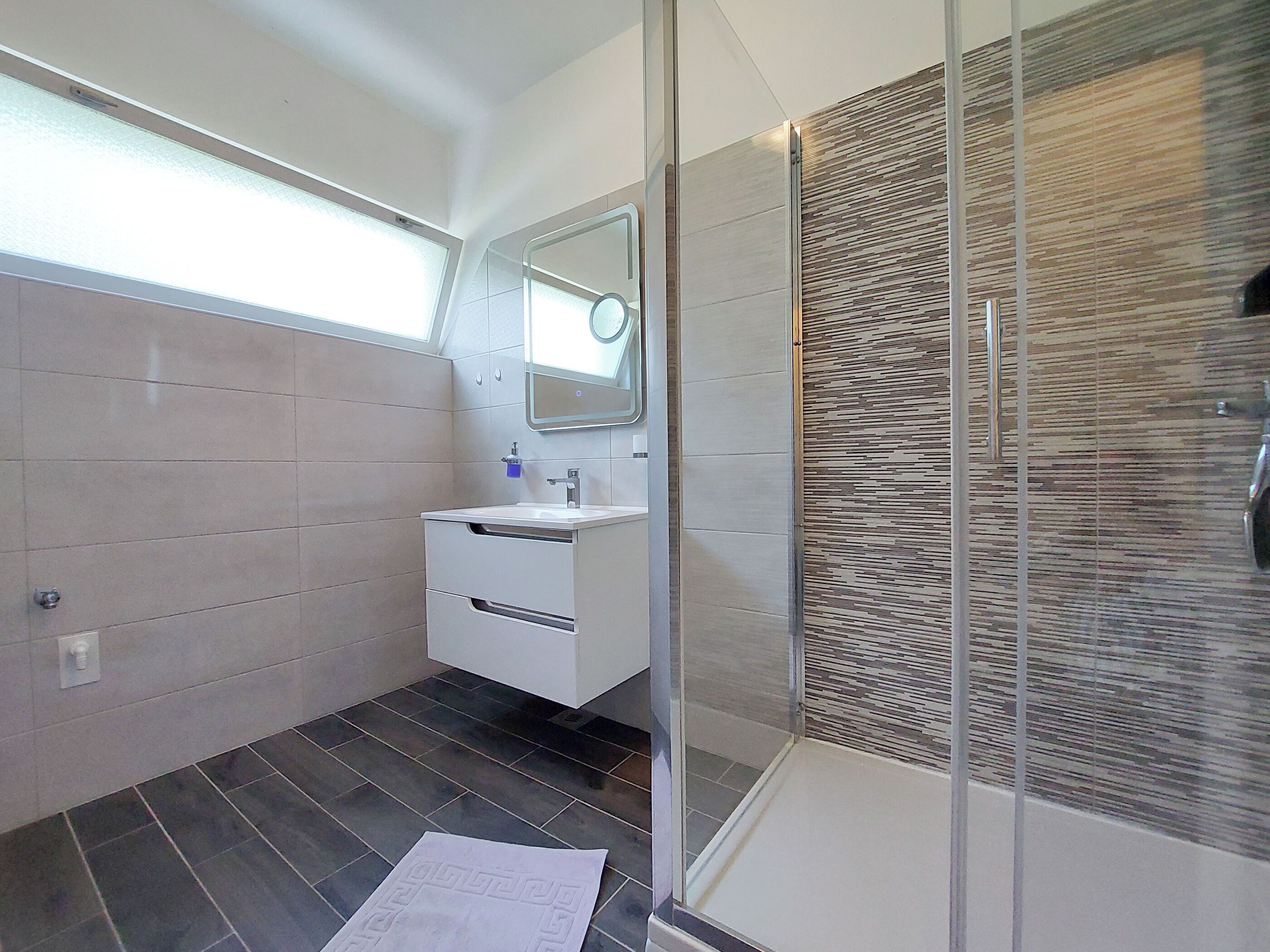 A modern bathroom with a glass shower enclosure, a white sink, and a mirror above it.