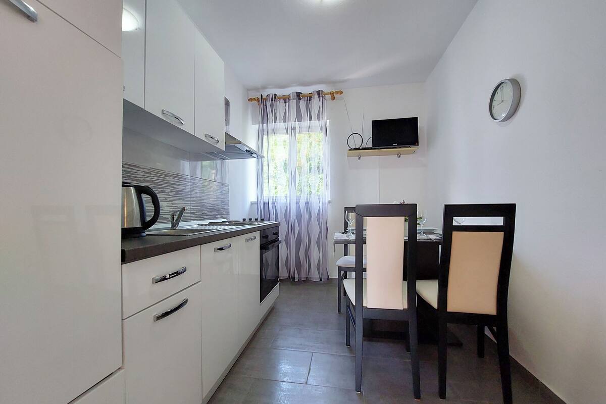 A compact kitchen with white cabinets, a stove, a sink, and a dining area with two chairs and a table.