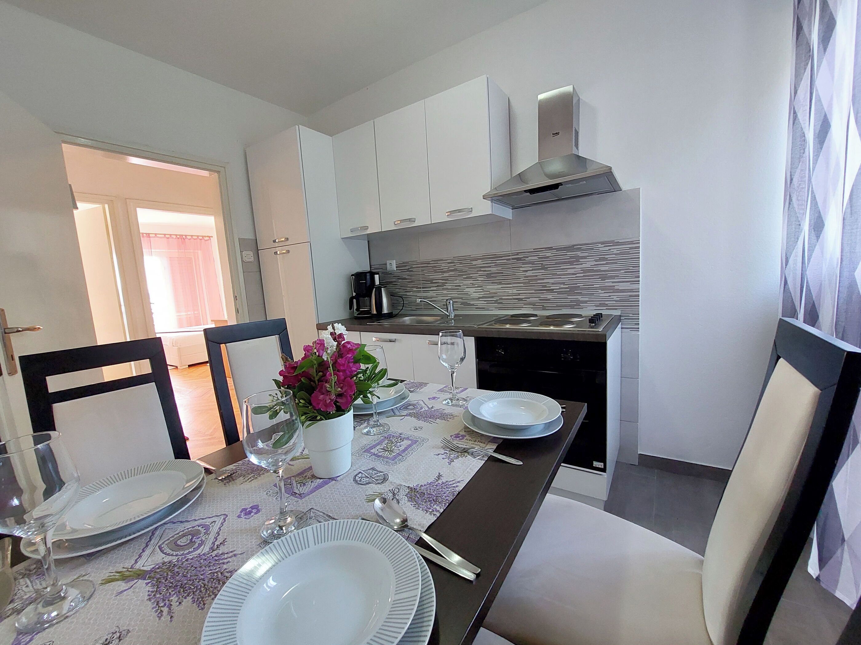Una cocina moderna con armarios blancos, campana extractora de acero inoxidable y salpicadero de azulejos.