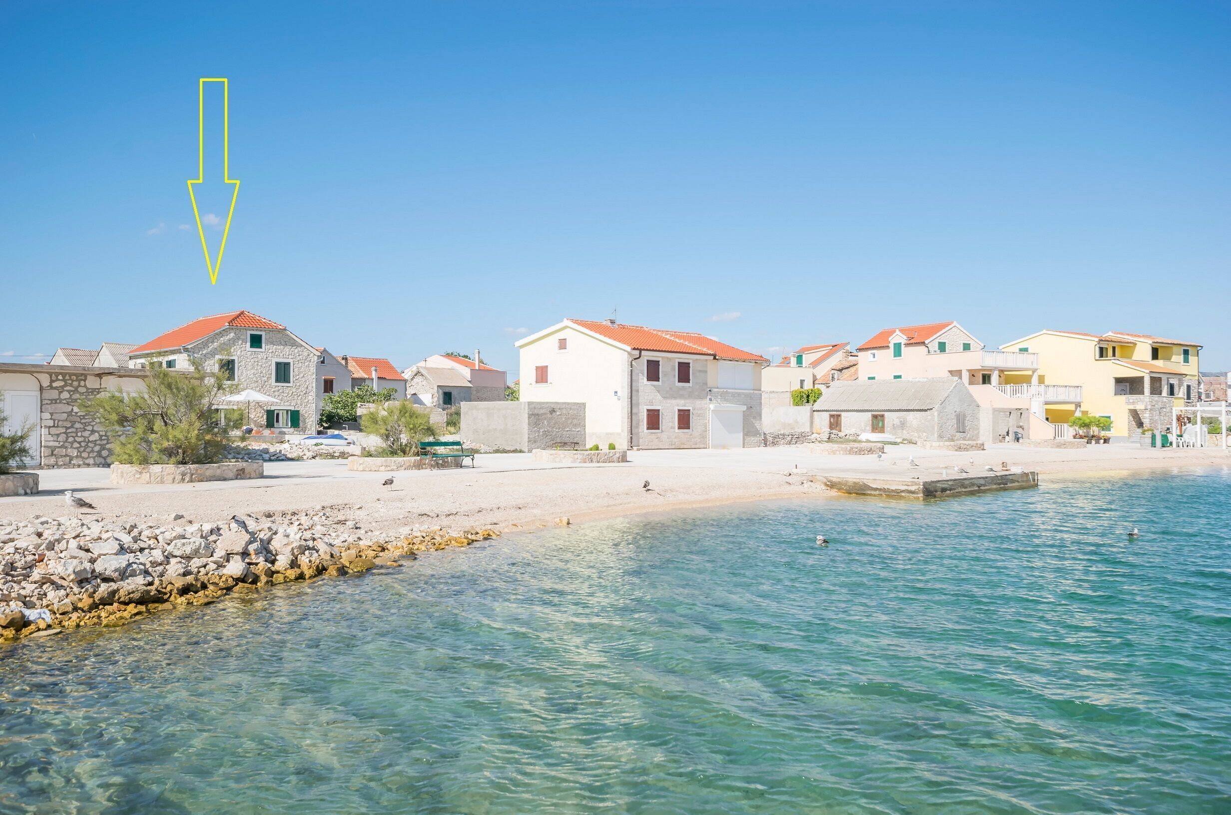 Ein Küstdorf mit Steinhäusern, einem Sandstrand und klarem, blauem Wasser.