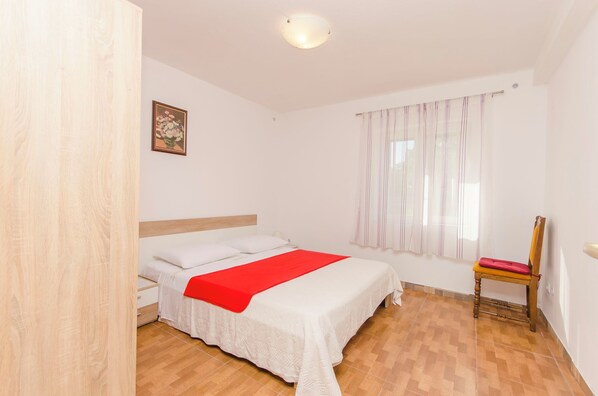 A bedroom with a bed, a chair, and a window with curtains. - Apartment Island Sun Terrace (Sibenik)