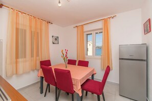 A dining area with a table set for six, red chairs, a refrigerator, and a window with curtains. - Apartment Island Sun Terrace (Sibenik)