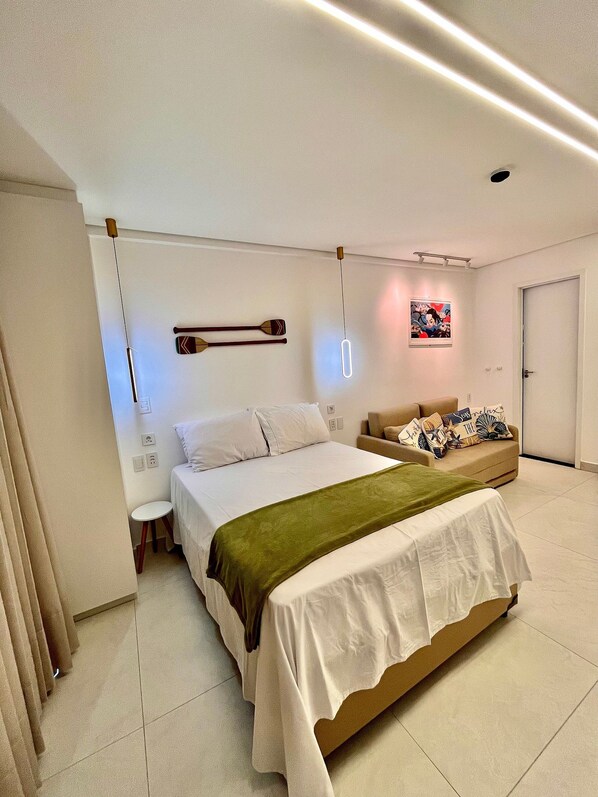 A modern bedroom with a bed, bedside table, and a sofa. - Beach Class Verano - Porto de Galinhas (Ipojuca)