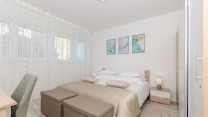A modern bedroom with a bed, two ottomans, a chair, a nightstand, and artwork on the wall. - Apartment Astrid (Split)