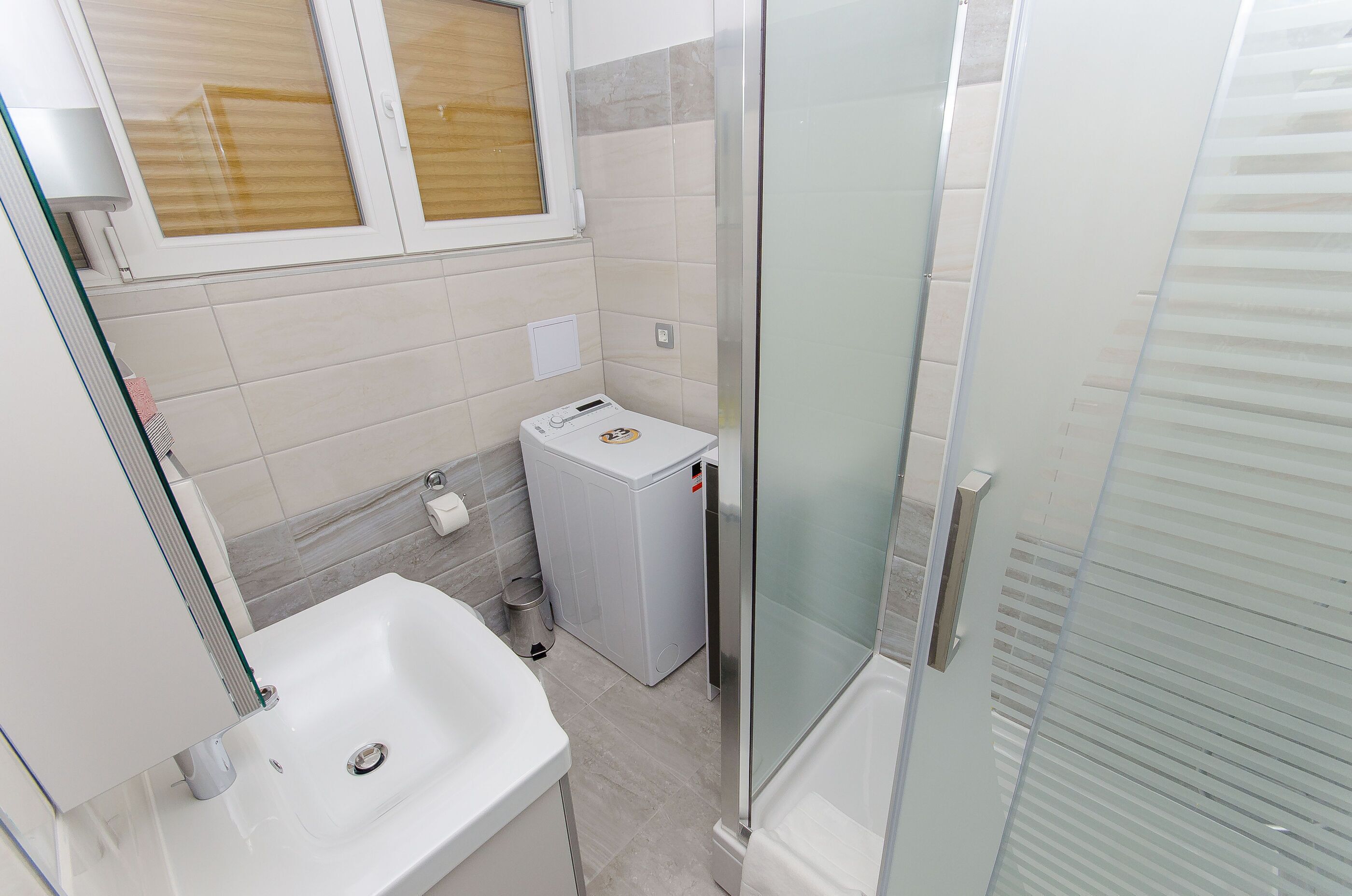 A bathroom with a white sink, a small washing machine, and a glass shower enclosure.