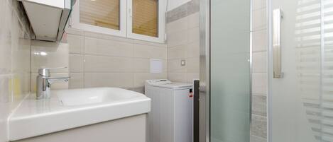 A modern bathroom with a sink, a washing machine, and a glass shower enclosure.
