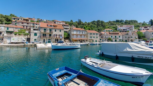 A harbor with boats docked, stone buildings with red-tiled roofs, and a clear blue sky. - Apartment Pavlimir (Solta)