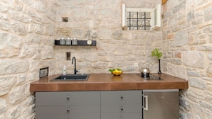 A stone-walled kitchen with a sink, a clock, and a small window. - Apartment Pavlimir (Solta)