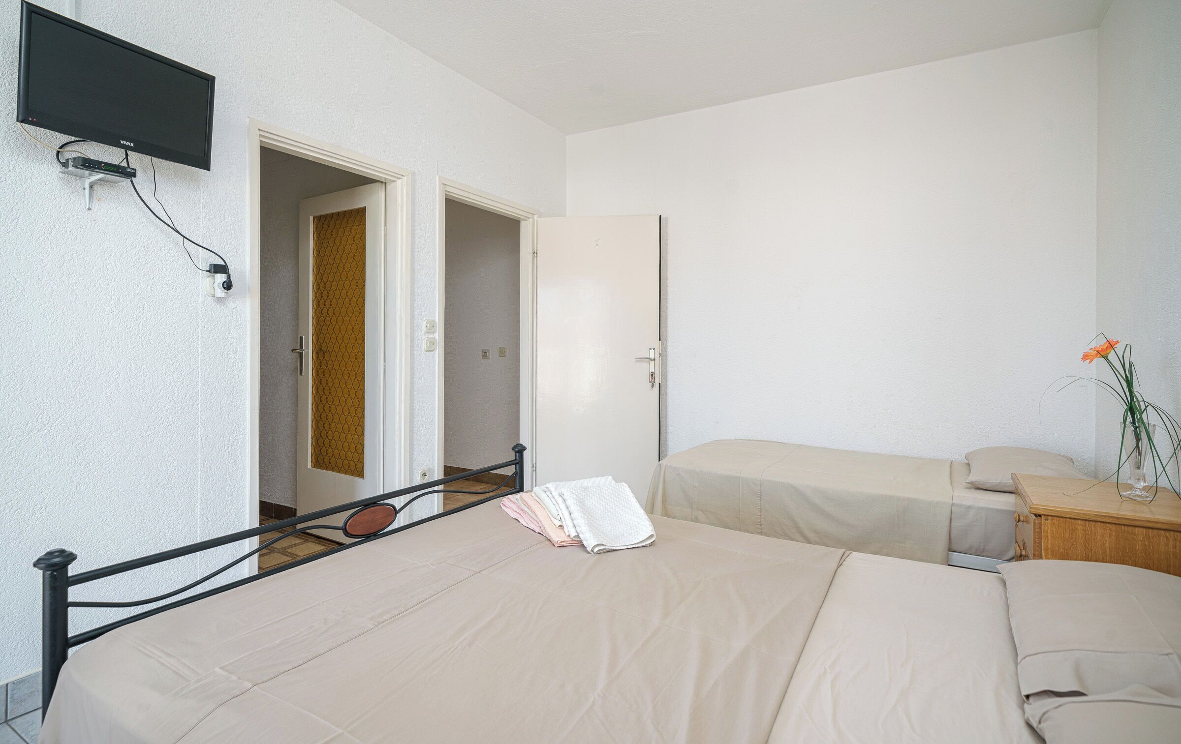 Una camera d'albergo con un letto, un comodino, una TV fissata al muro e una porta che dà su un'altra stanza.