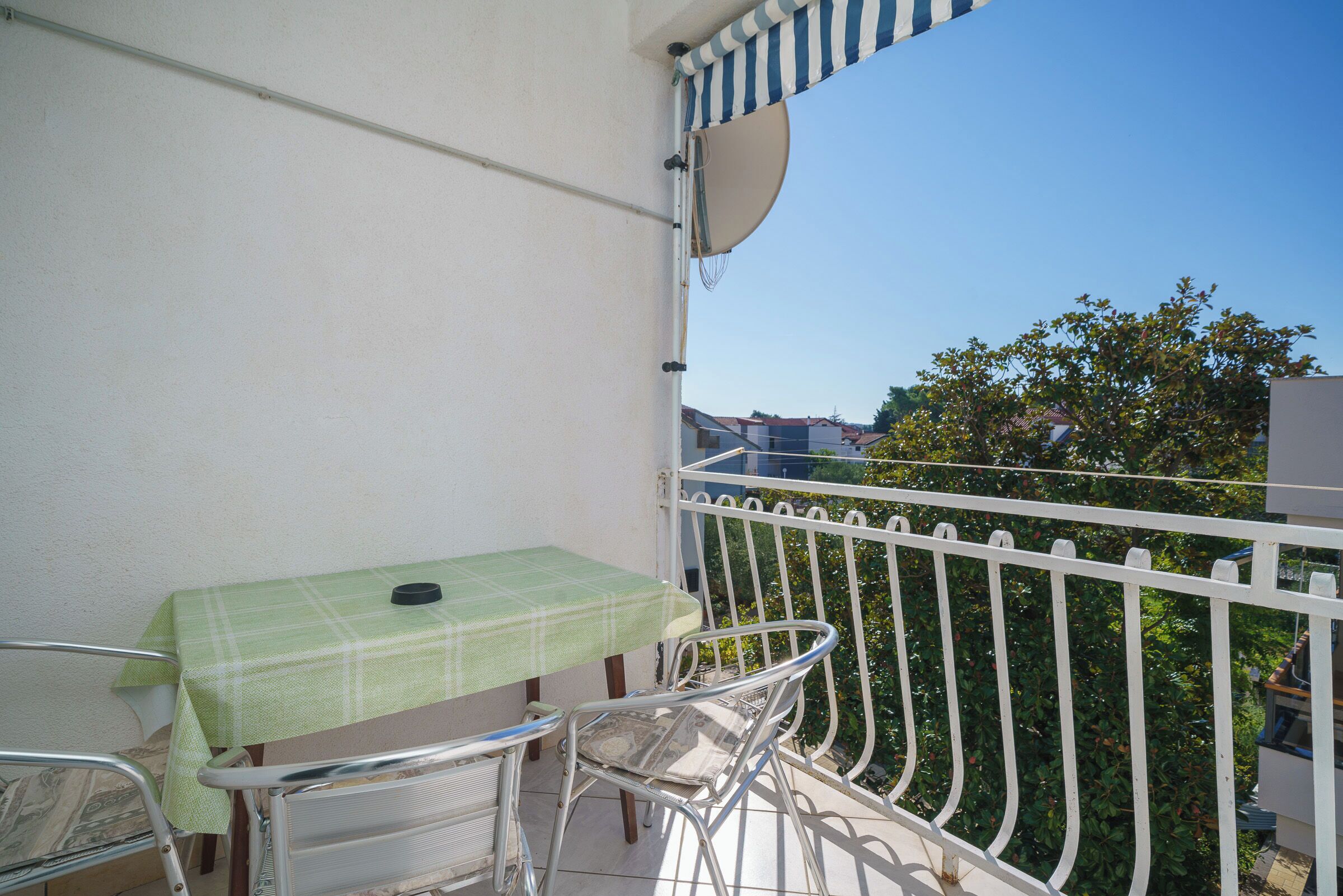 Un balcon avec une table et des chaises, une balustrade blanche et une vue sur les arbres et les bâtiments.