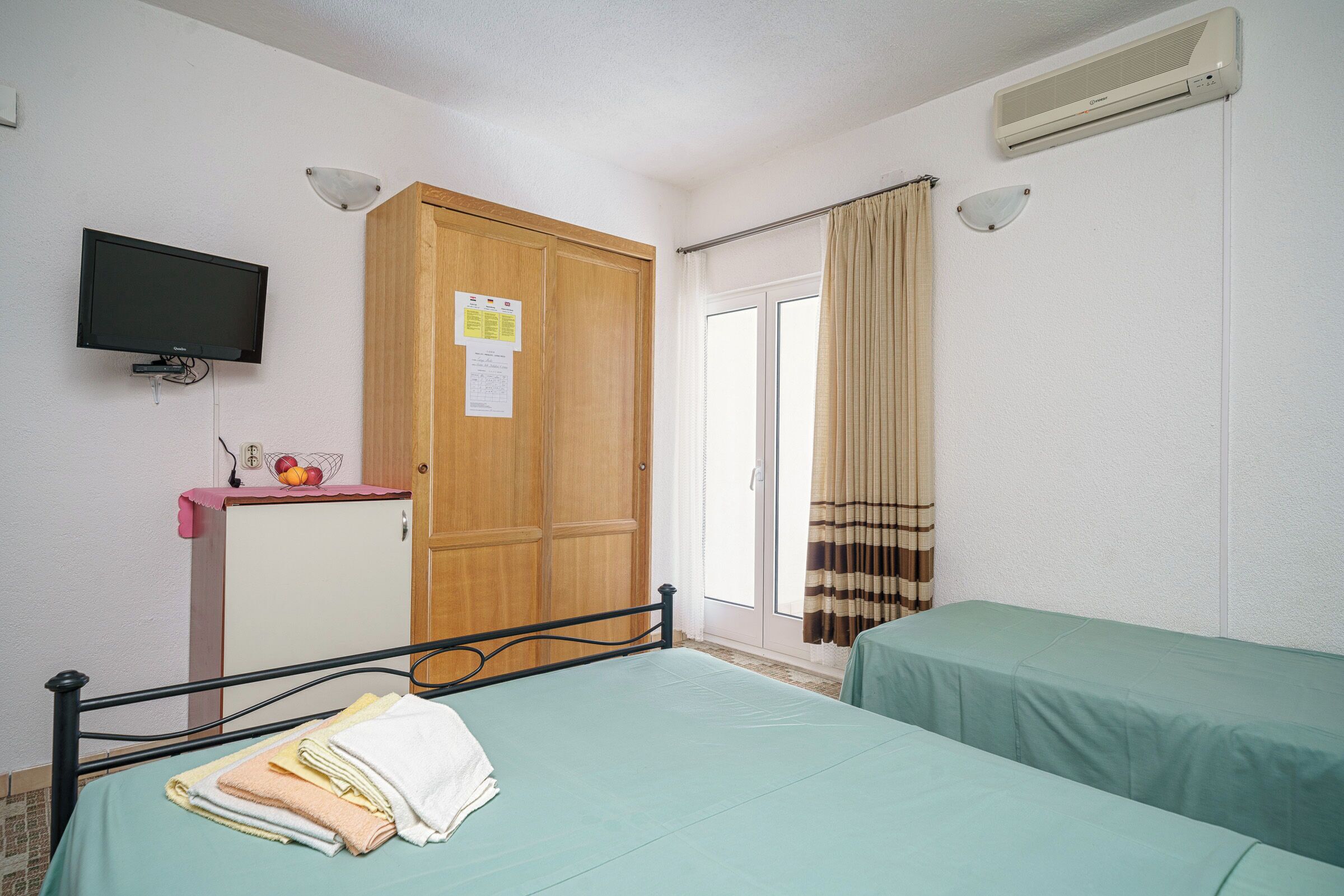 Ein Zimmer mit Bett, Fernseher, Kleiderschrank und einer Schiebetür.