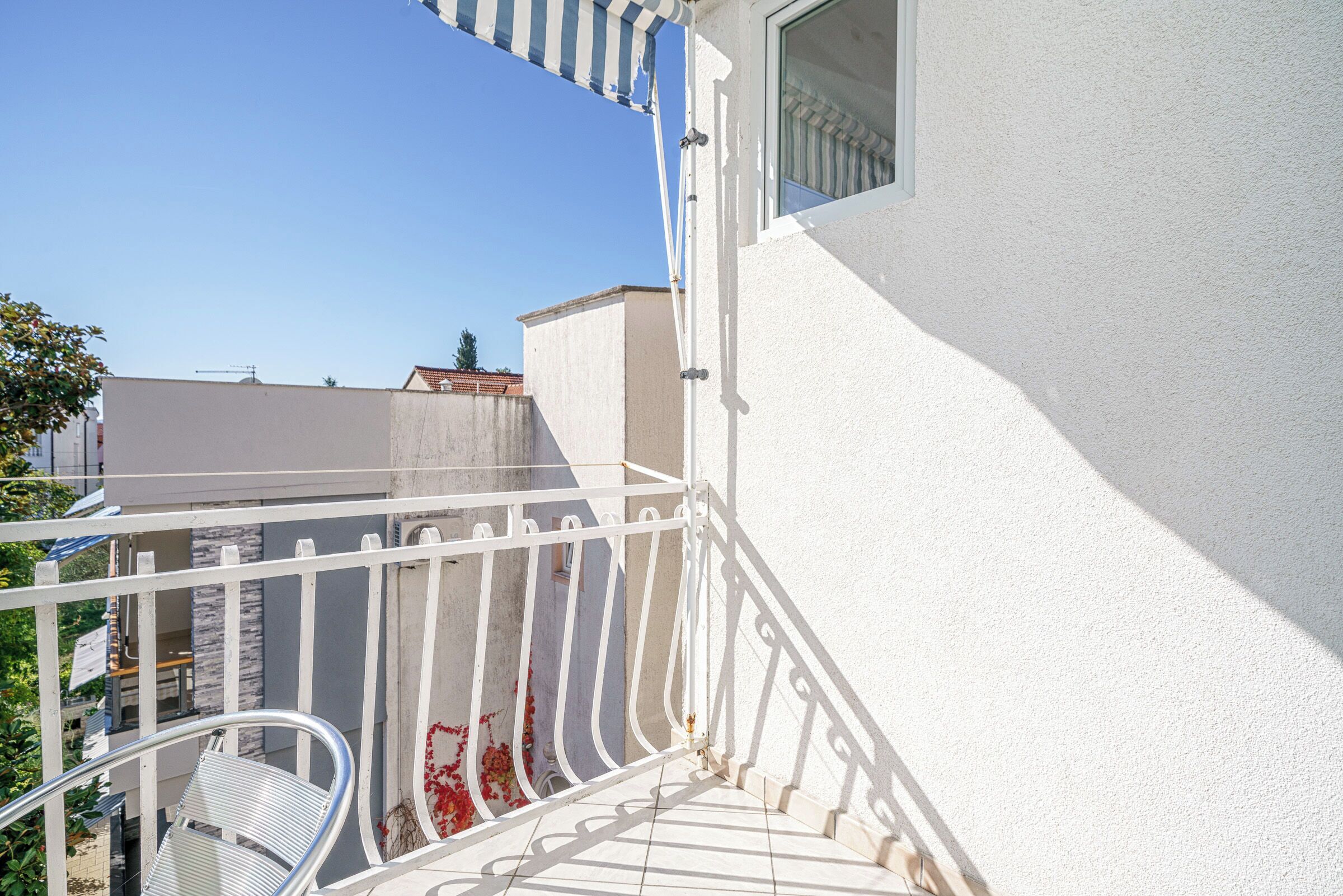A white balcony with a metal railing, a white chair, and a window.
