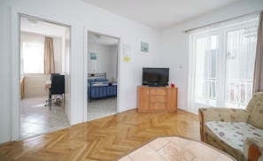 A room with a wooden herringbone floor, a television on a wooden cabinet, a bed with blue bedding, and a patterned armchair. - Apartments Villa Sunset (Vodice)