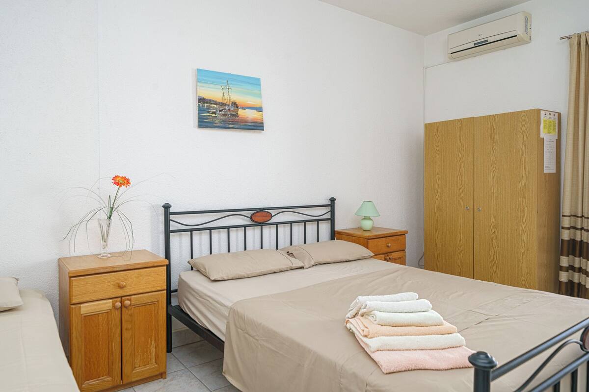 A bedroom with a bed, wooden nightstands, a small table with a lamp, a wardrobe, and a painting on the wall.