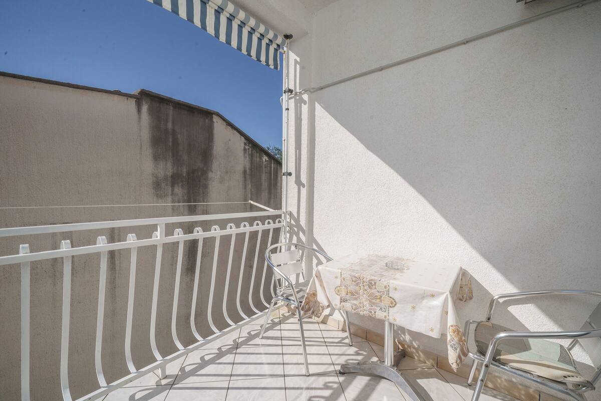 A balcony with a white railing, a table with a patterned tablecloth, and a chair.