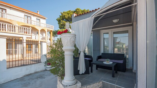 A balcony with a white column, a potted plant with red flowers, and a black sofa. - House Kala (Sibenik)