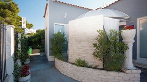 A modern building with a stone facade, a covered outdoor area with plants, and a satellite dish on the roof. - House Kala (Sibenik)
