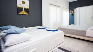 A modern bedroom with a white bed, a second bed, a dark wall with a painting, a wardrobe, and a window with blinds. - House Kala (Sibenik)