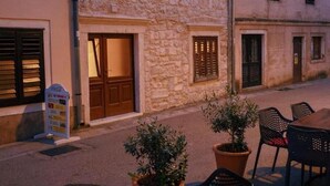 Un edificio de piedra con múltiples ventanas y puertas, y un área exterior con asientos y plantas en macetas.