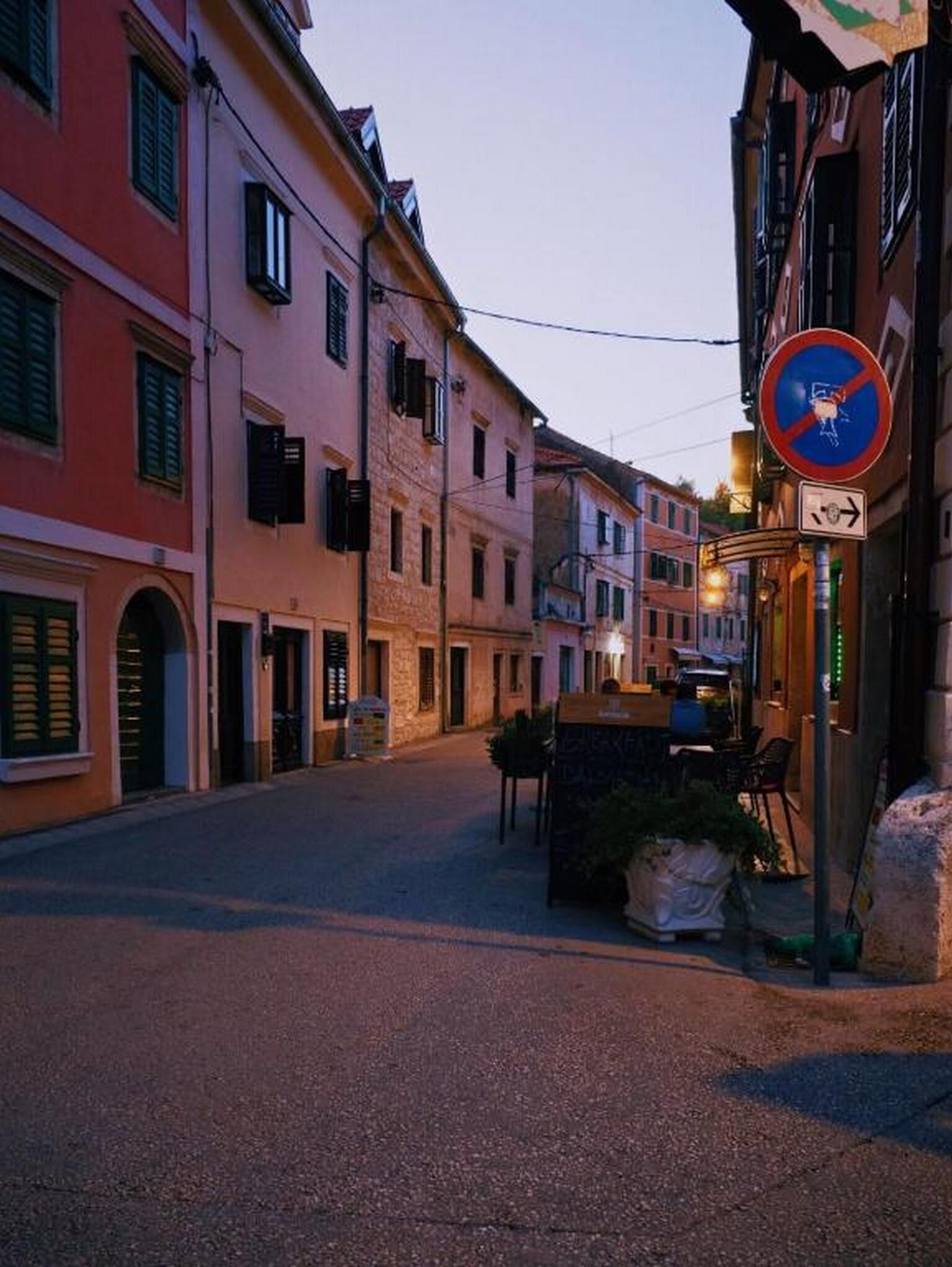 A quiet street with buildings, a no parking sign, and a directional arrow sign.