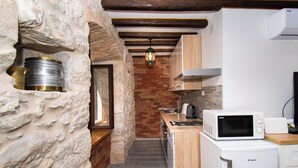 Una cocina con paredes de piedra, vigas de madera, microondas, tostadora y lavaplatos.