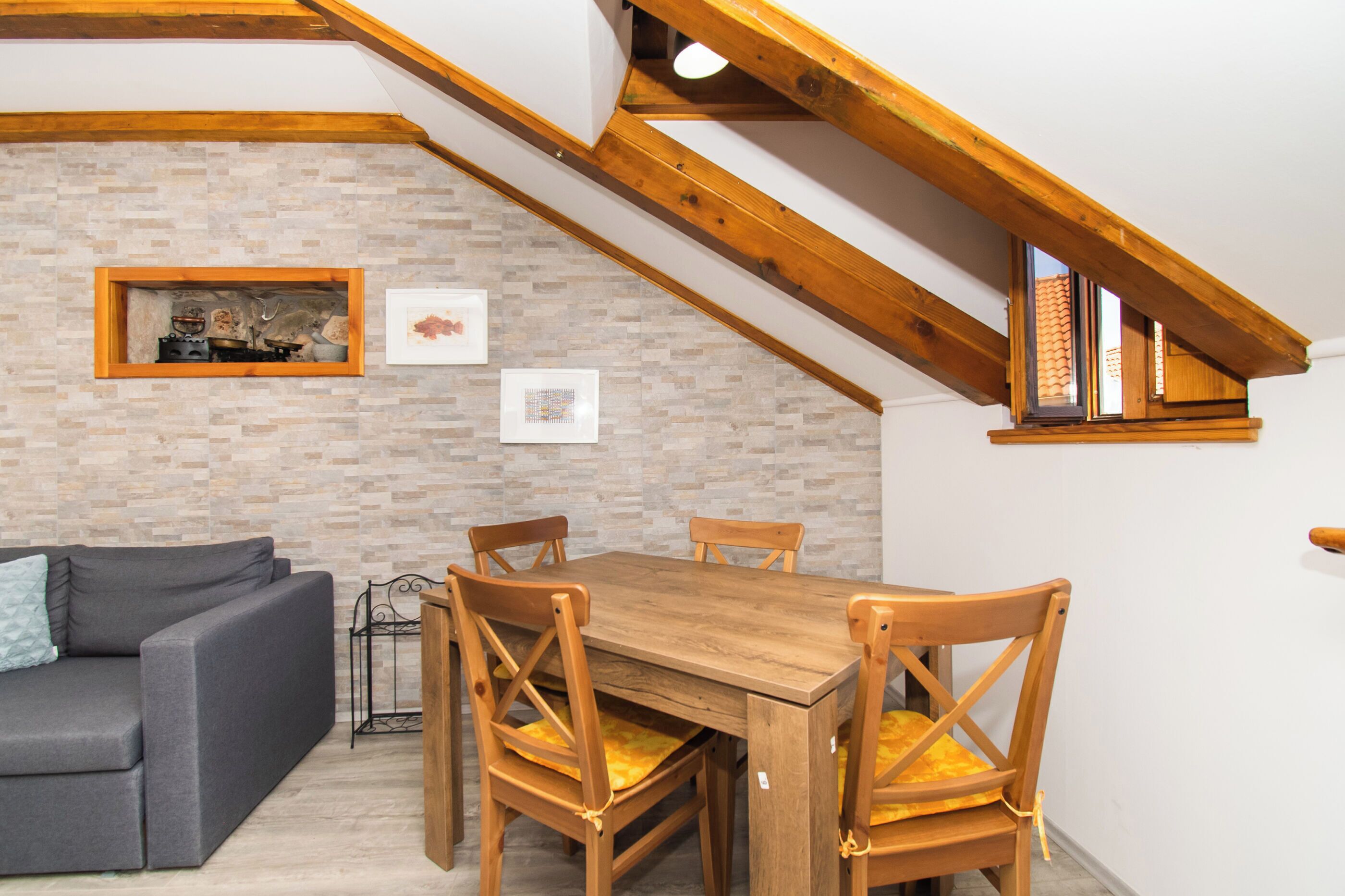 Ein Essbereich mit Holztisch und -stühlen, einem grauen Sofa und einer Backsteinwand mit gerahmten Bildern.