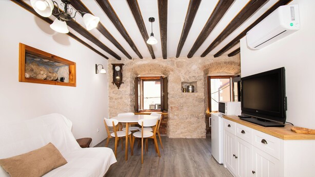 Una habitación acogedora con un sofá blanco, una mesa de comedor con sillas, un televisor en un mueble de madera y una pared de piedra.