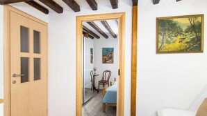 Una habitación con puerta de madera, una cama con colcha azul, una silla de madera y un cuadro en la pared.