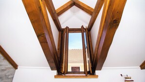 Una habitación con techo inclinado, vigas de madera, una ventana y un ventilador de techo.