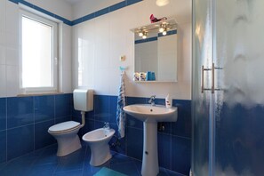 A bathroom with a toilet, bidet, and sink, featuring blue tiles and a window. - Apartments Anamarija (Rovinj)