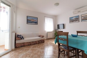 A living room with a sofa, a dining table with chairs, a TV, and a window with curtains. - Apartments Anamarija (Rovinj)