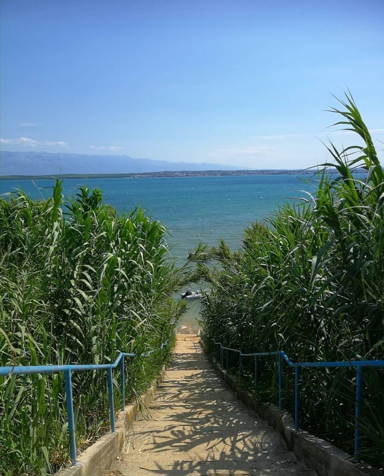 A pathway leading to a beach with a clear view of the sea and distant mountains.
