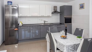 Een moderne keuken met grijze kastjes, een roestvrijstalen koelkast en een eethoek met een tafel gedekt voor twee personen.