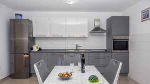 Een moderne keuken met een marmeren aanrecht, een eettafel met stoelen, een koelkast, een fornuis en kastjes.