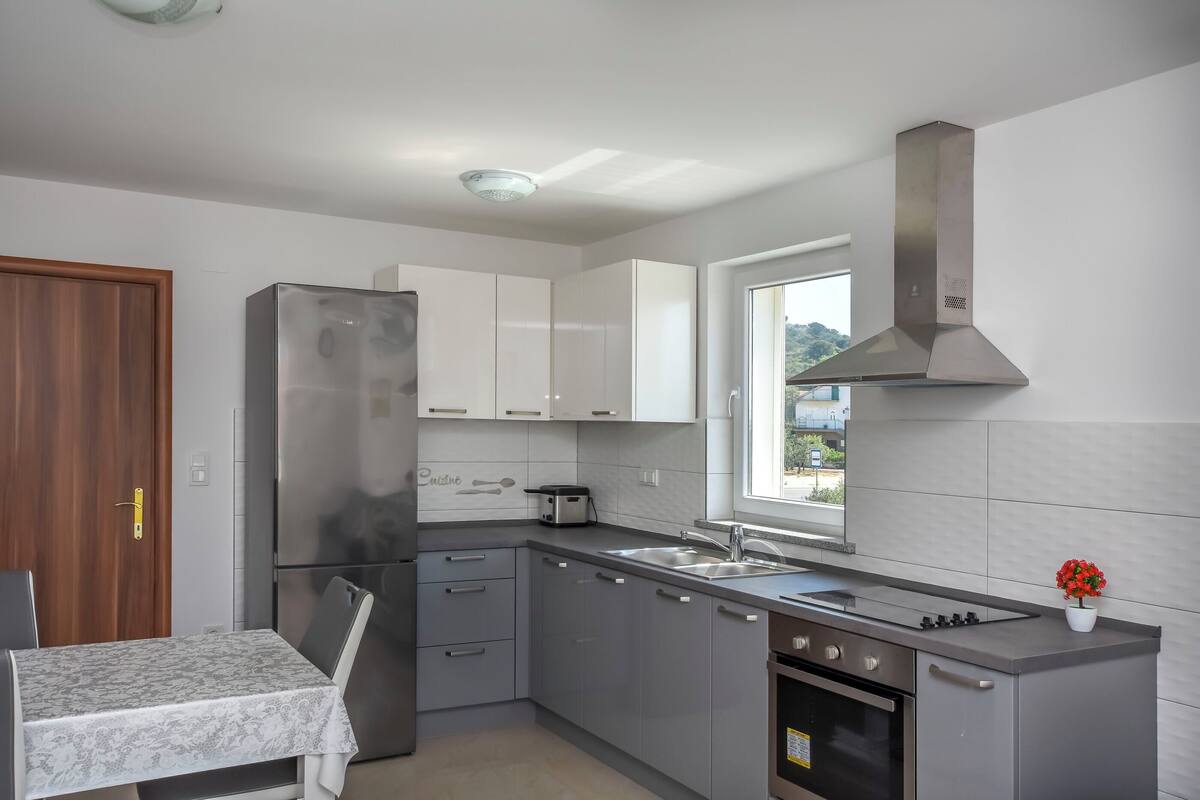 A modern kitchen with a built-in oven, a stainless steel refrigerator, and a window providing natural light.