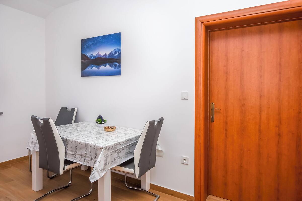 A dining area with a table and chairs, a wooden door, and a wall-mounted picture.