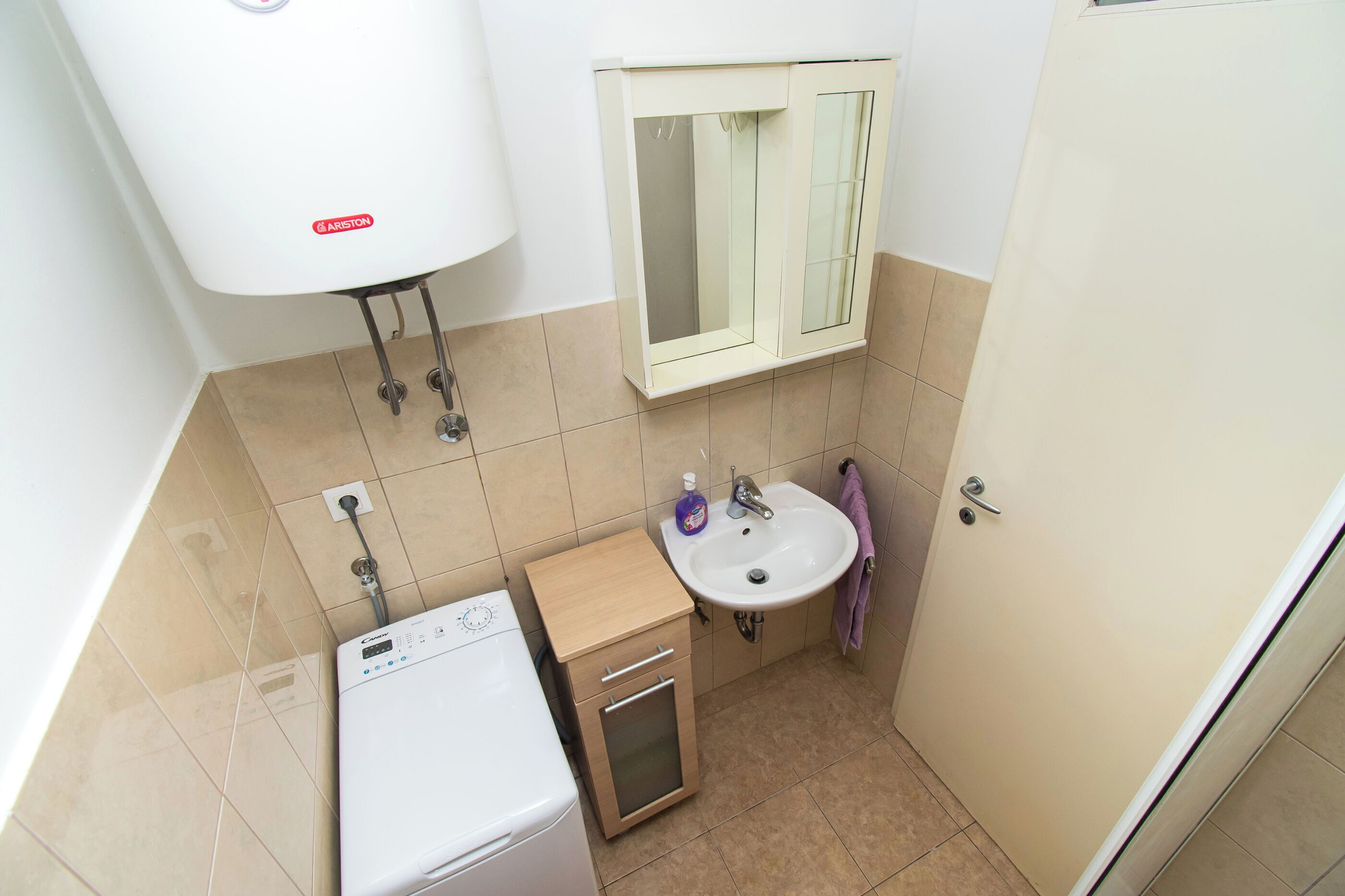 A compact bathroom with a white toilet, a sink, a mirror, and a washing machine.