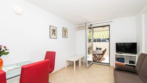 Ein modernes Wohnzimmer mit Glastisch, roten Sesseln, einer Couch, einem Fernseher und einer Schiebetür zu einer Terrassenförmigen Außenanlage.