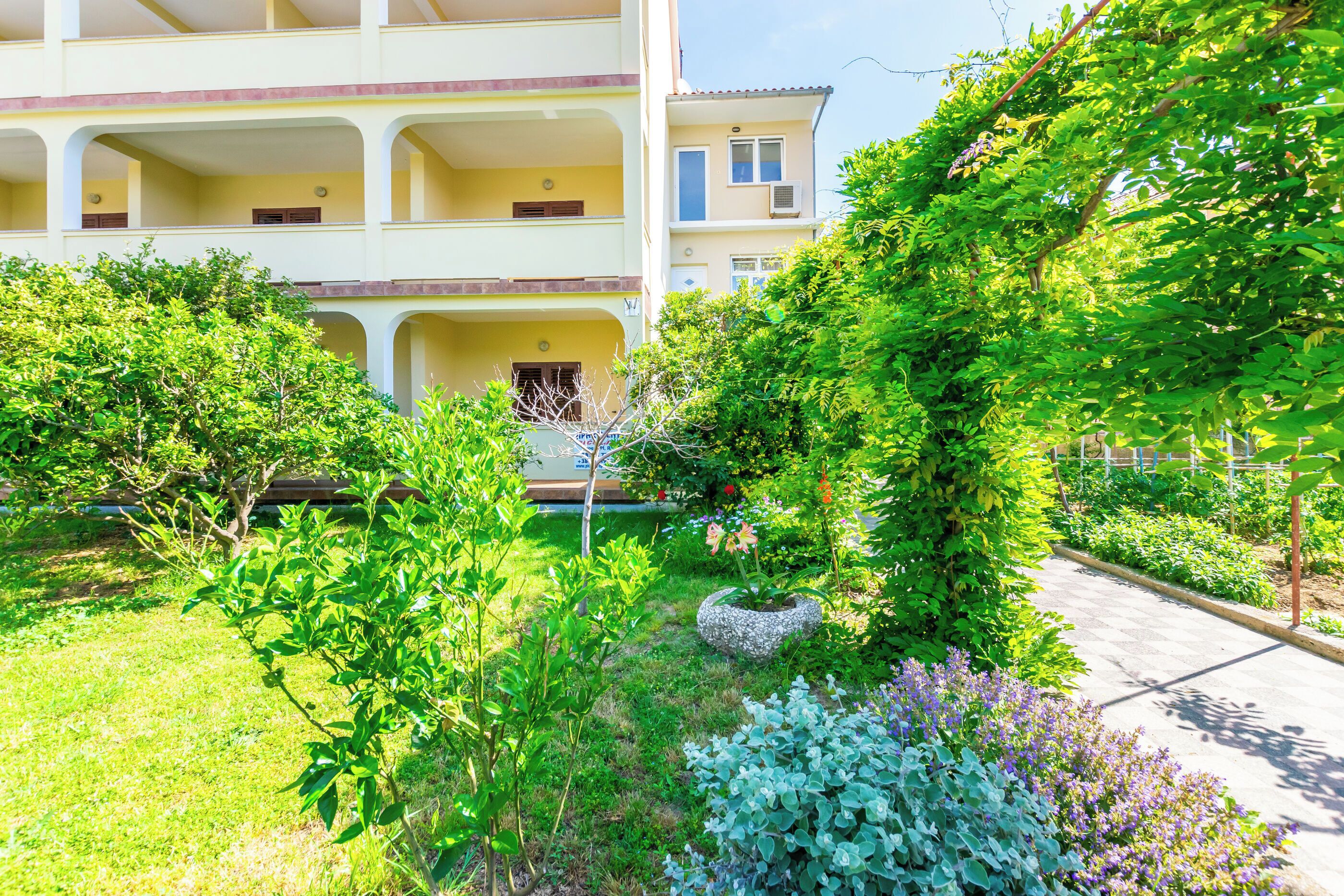 A multi-story building with balconies, surrounded by lush greenery and a garden area.