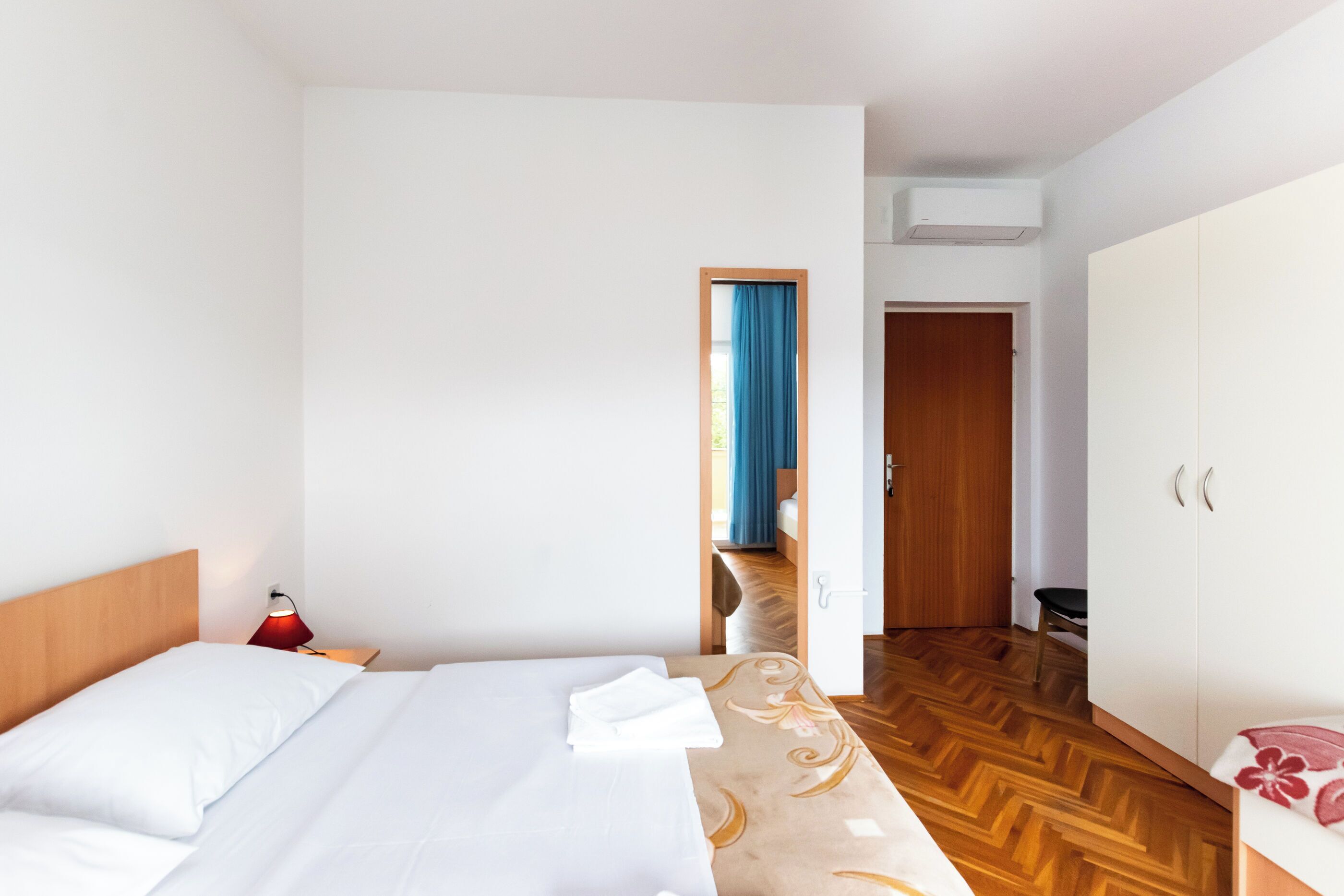 A hotel room with a bed, a nightstand with a lamp, a wardrobe, and a wooden floor.