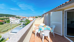 A balcony with a table and chairs, a tiled floor, and a view of a residential area. - Apartments Ivan i Marija (Lopar)