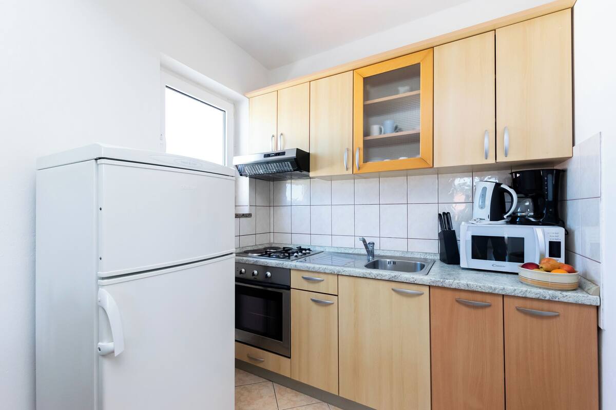 Une cuisine de taille réduite équipée d’un réfrigérateur, d’une cuisinière, d’un four à micro-ondes et de meubles de rangement en bois.