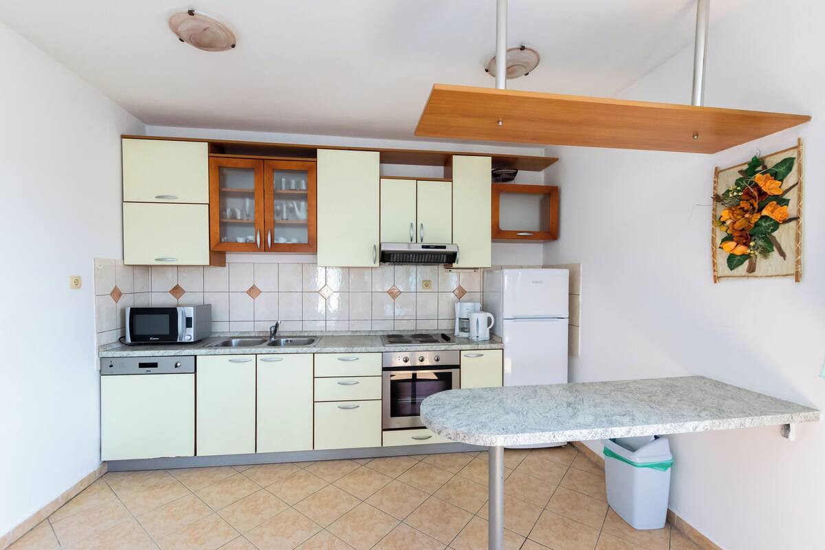 Une cuisine de taille réduite avec des meubles de couleur vert clair, un four à micro-ondes, une cuisinière et un évier.
