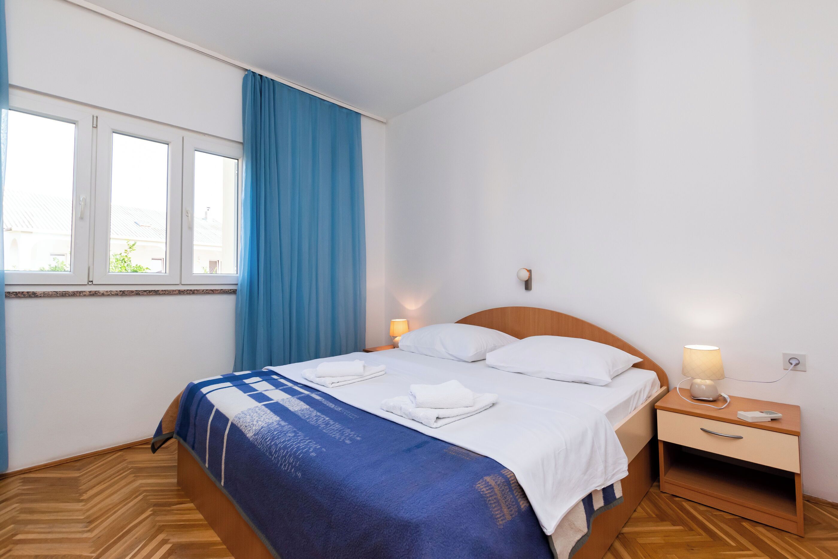 Una camera d'albergo con un letto, un comodino, una lampada e una finestra con tende.