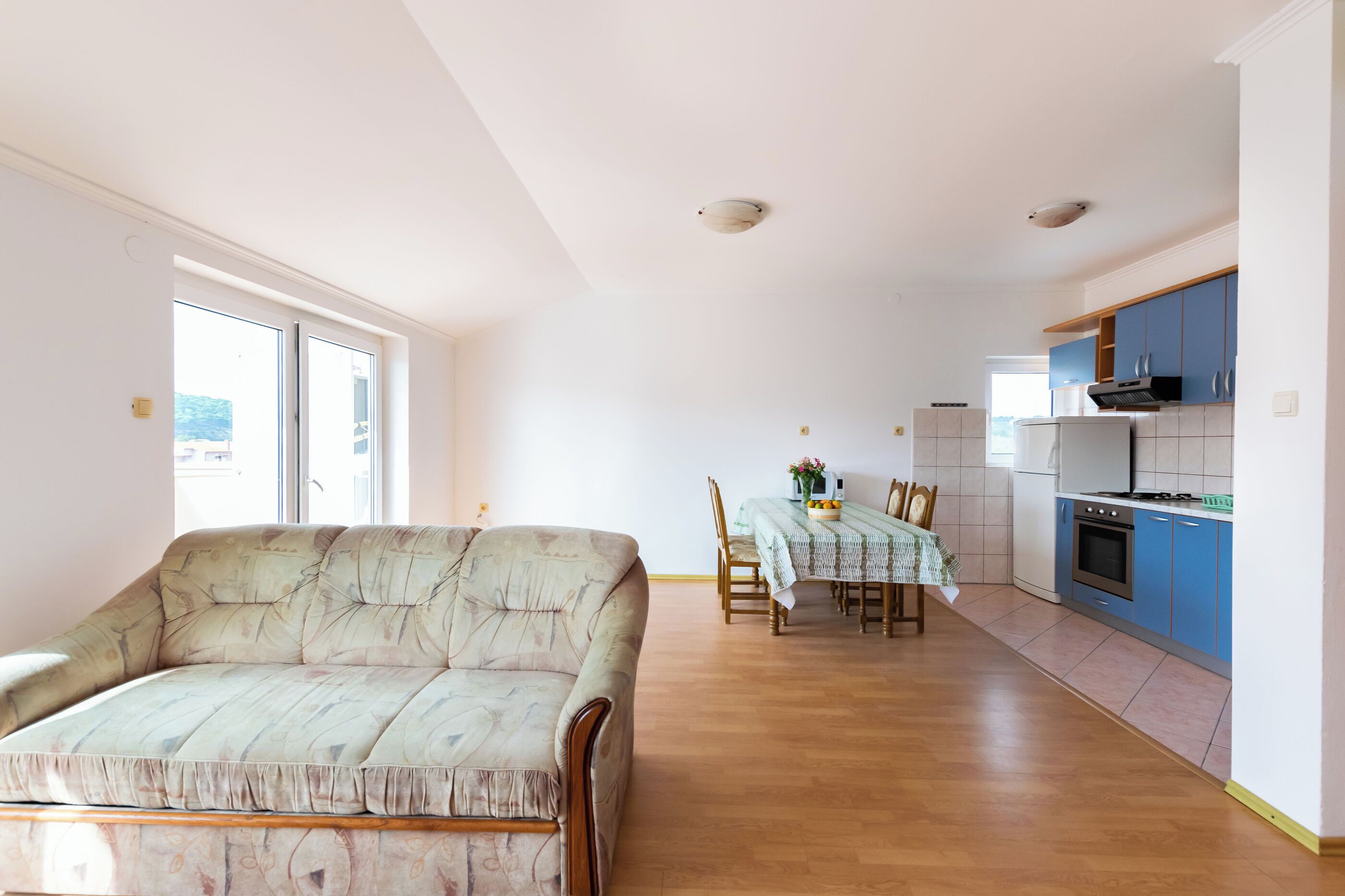 Ein geräumiger Wohnbereich mit einer Couch, einem Esstisch mit Stühlen und einer Küchenzeile mit Schränken und Geräten.