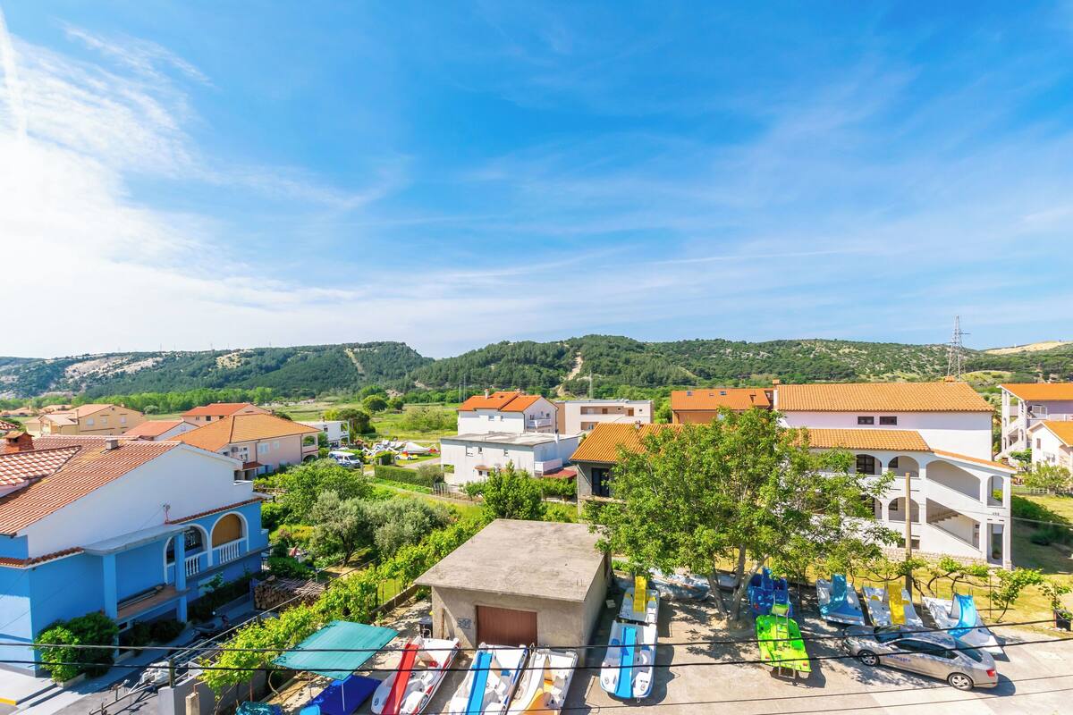 Un village côtier doté d’une architecture méditerranéenne traditionnelle, avec des bâtiments aux toits de tuiles rouges et une place centrale où sont amarrés des bateaux aux couleurs vives.