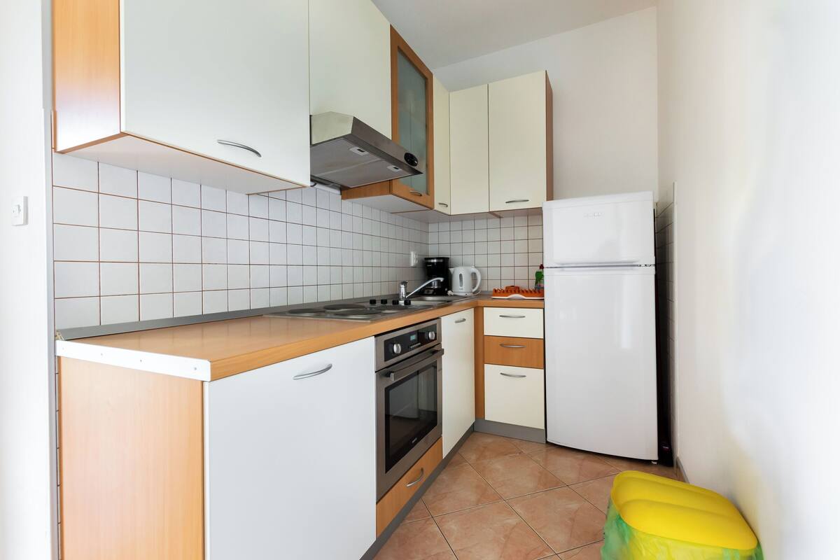 Une cuisine de taille réduite avec des meubles blancs, une cuisinière, un évier et un réfrigérateur.